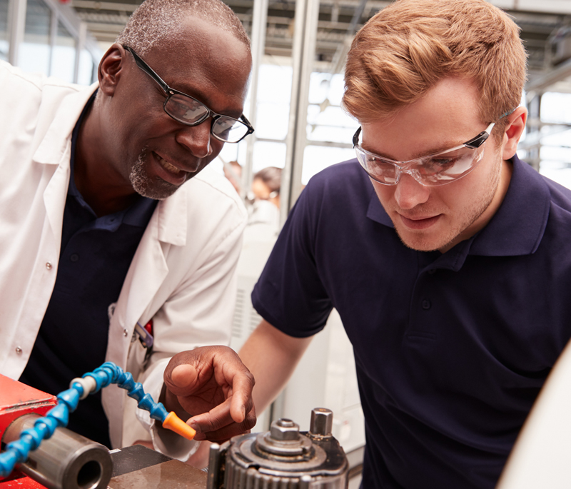 A photograph of an employee teaching a trainee show to use machinery equipment